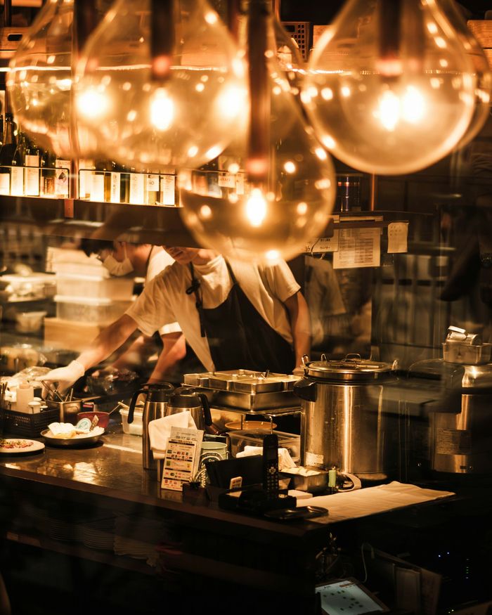 Cooks at work behind a long counter, under warm hanging lamps